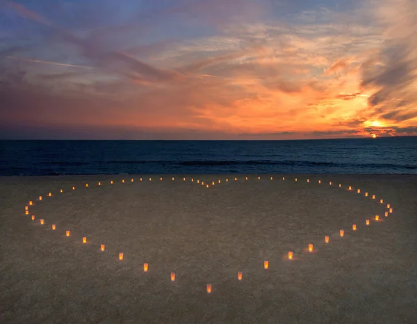 Свечи сердце на пляже песчаного моря против Яркий закат — стоковое фото