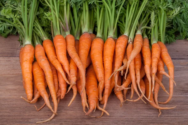 Связка свежей моркови с зелеными листьями по деревянному фону — стоковое фото