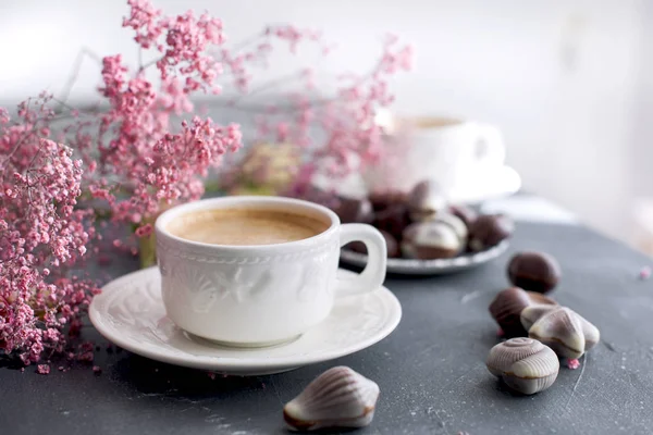 Шоколадные конфеты в форме ракушки и две чашки ароматного кофе. Романтический завтрак. Светлые цвета. Розовые цветы. Свободное место для текста. копией пространства — стоковое фото